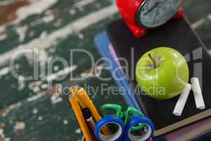 Alarm clock, apple and chalk on stack of books with pen holder