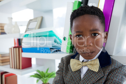Close up portrait of boy imitating as businessman standing by shelf