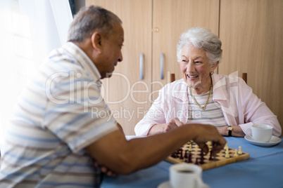 Smiling male and female seniors playing chess at table