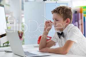 Confident serious businessman with pen working on laptop