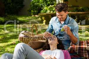 Man feeding grape to woman in park