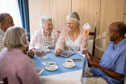 Happy senior people enjoying tea while playing cards