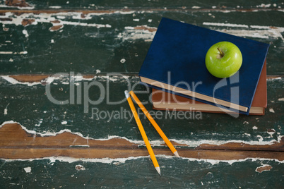 Apple on stack of books with pencils