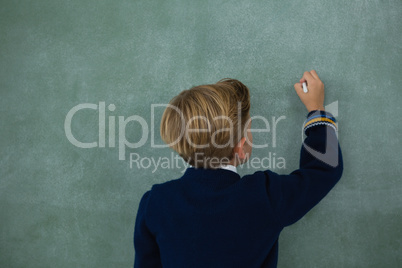 Schoolboy writing with chalk on chalkboard