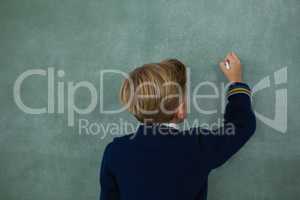 Schoolboy writing with chalk on chalkboard