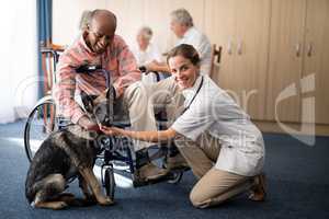 Portrait of female doctor kneeling by disabled senior man stroking puppy