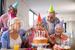 Friends looking at senior man blowing birthday candles