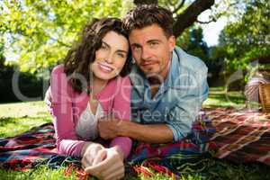 Portrait of smiling couple lying on picnic blanket in park