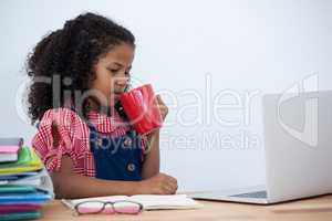 Businesswoman having coffee while looking at laptop