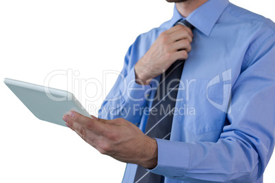 Mid section of businessman adjusting necktie while holding tablet