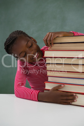 Schoolgirl sitting with books stack against chalkboard