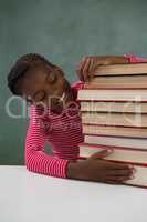 Schoolgirl sitting with books stack against chalkboard