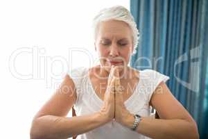 Senior woman praying with eyes closed against window
