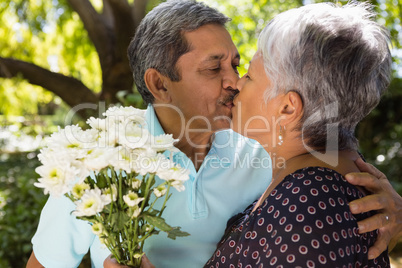 Senior man kissing while giving flowers to woman