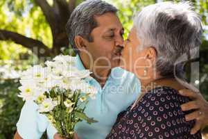 Senior man kissing while giving flowers to woman