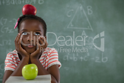 Schoolgirl sitting with red apple on her head against chalkboard