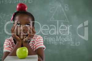 Schoolgirl sitting with red apple on her head against chalkboard