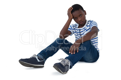 Sad boy sitting with hand on head against white background