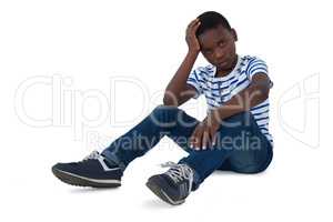 Sad boy sitting with hand on head against white background