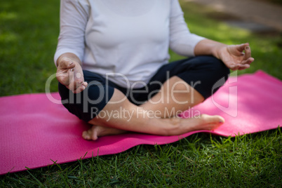 Mid section of senior woman meditating on exercise mat