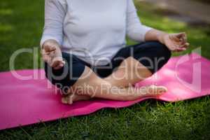 Mid section of senior woman meditating on exercise mat