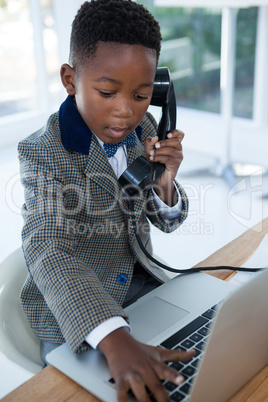 Businessman typing on laptop while using telephone