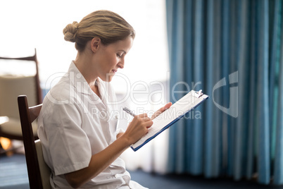 Side view of young female doctor writing on clipboard