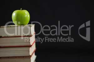 Green apple on book stack against black background