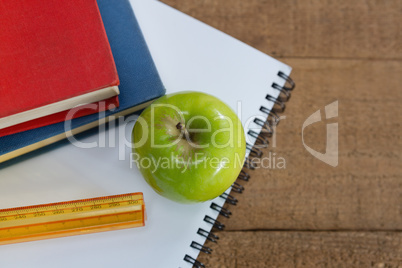 Green apple and school supplies on wooden table