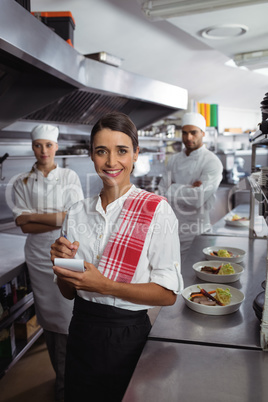 Waitress standing with kitchen staff in commercial kitchen