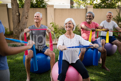 Senior people listening to trainer while exercising with ribbons and balls