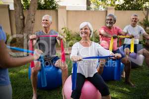 Senior people listening to trainer while exercising with ribbons and balls