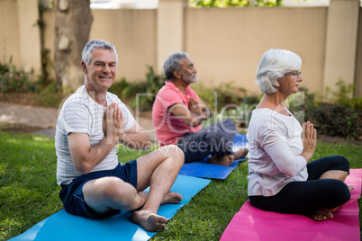 Smiling senior man meditating in prayer position with friends