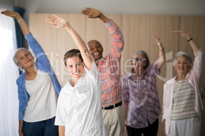 Portrait of smiling female doctor and seniors exercising with arms raised