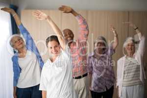 Portrait of smiling female doctor and seniors exercising with arms raised