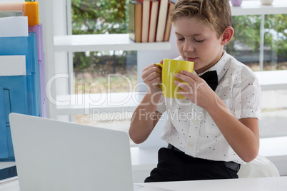 Businessman drinking coffee from yellow mug by laptop