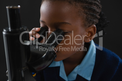 Schoolgirl using microscope against black background