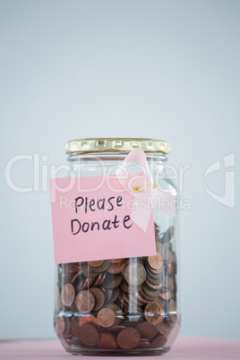 Close-up of card and pink Breast Cancer Awareness ribbon on jar with coins