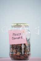 Close-up of card and pink Breast Cancer Awareness ribbon on jar with coins