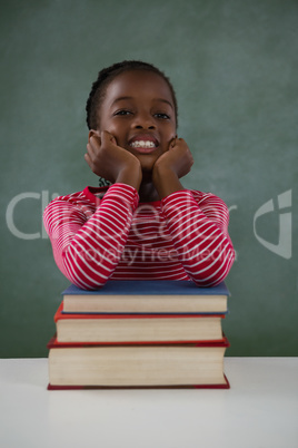 Schoolgirl leaning on books stack against chalkboard in classroom