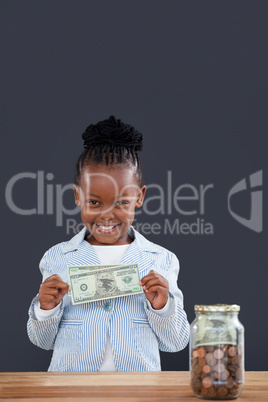 Portrait of smiling businesswoman with jar at desk showing paper currency