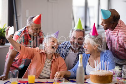 Cheerful senior woman taking selfie with friends at party