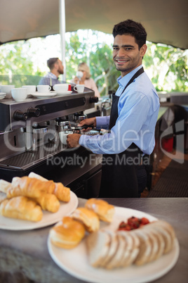 Smiling waiter making cup of coffee from espresso machine