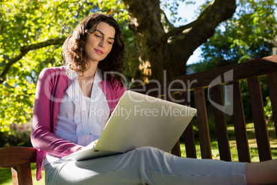 Woman sitting on bench and using laptop in garden on a sunny day