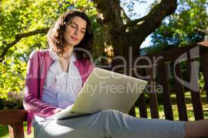 Woman sitting on bench and using laptop in garden on a sunny day