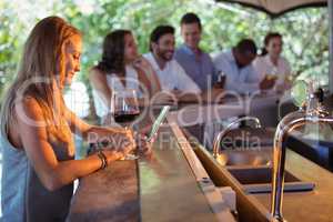 Smiling woman using mobile phone while having a glass of wine