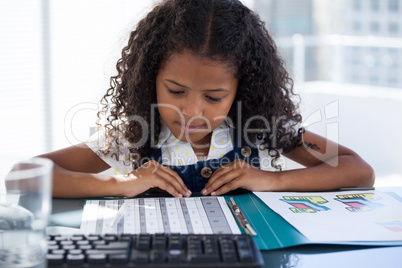 Businesswoman reading file while sitting at desk