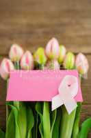 Close-up of pink Breast Cancer Awareness ribbon with blank card on fresh tulips