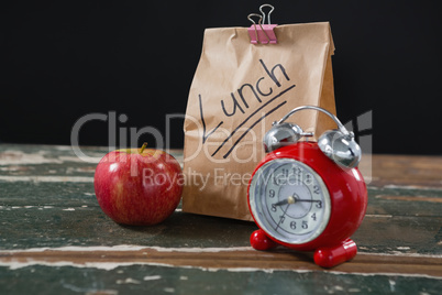 Apple, alarm clock and lunch bag on wooden table