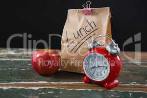 Apple, alarm clock and lunch bag on wooden table